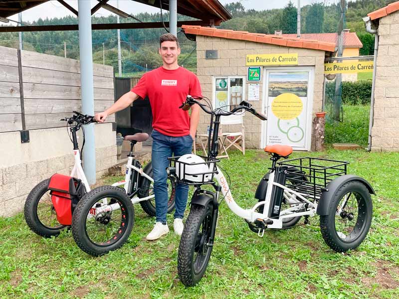 Triciclos eléctricos para alquiler con joven a punto de montar en uno de ellos en Carreño
